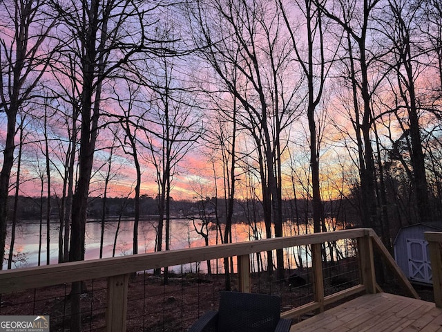 deck at dusk with an outdoor structure, a water view, and a storage shed