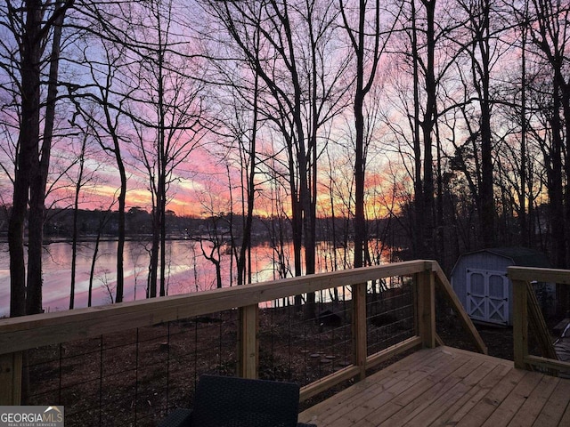 deck at dusk with an outbuilding, a storage shed, and a water view