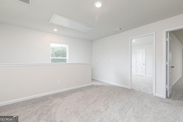 empty room featuring carpet flooring, baseboards, visible vents, and attic access