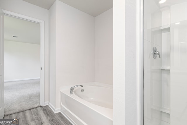 bathroom featuring walk in shower, baseboards, a garden tub, and wood finished floors