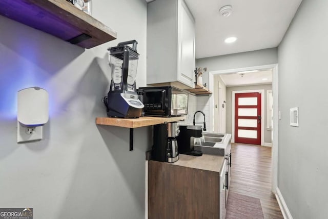 interior space featuring white cabinets, black microwave, a sink, light countertops, and dark wood-style floors
