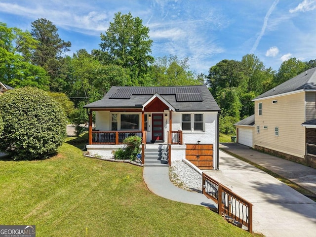 bungalow with a porch, brick siding, an outdoor structure, roof mounted solar panels, and a front lawn