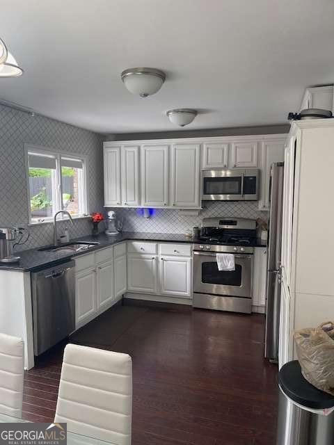 kitchen with white cabinets, dark countertops, appliances with stainless steel finishes, a sink, and decorative backsplash