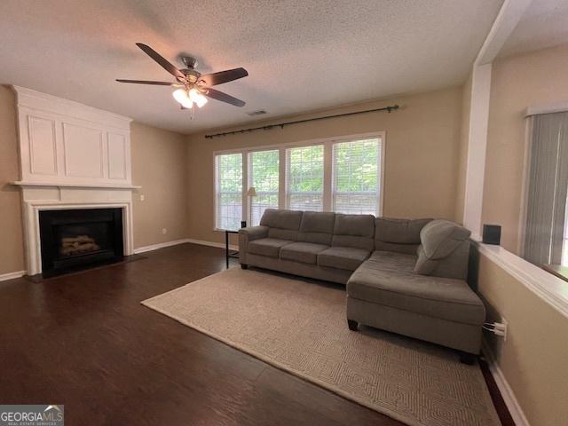 living area featuring ceiling fan, a textured ceiling, a fireplace, baseboards, and dark wood-style floors