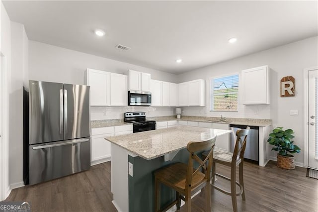 kitchen featuring white cabinets, appliances with stainless steel finishes, a kitchen bar, a kitchen island, and visible vents