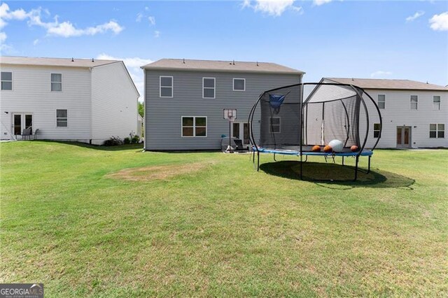 back of house with a lawn and a trampoline