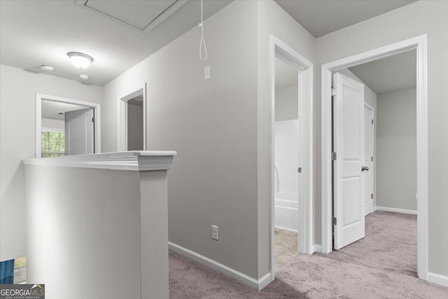 hallway featuring baseboards, attic access, and carpet