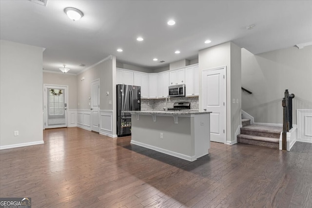 kitchen with crown molding, stainless steel appliances, white cabinetry, a kitchen bar, and dark wood-style floors