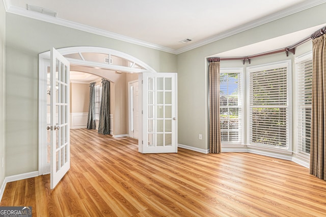spare room with crown molding, arched walkways, french doors, and light wood-type flooring