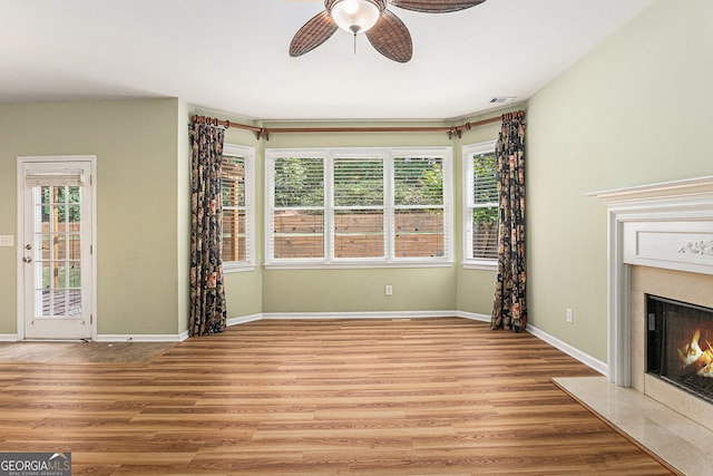 unfurnished living room featuring a premium fireplace, ceiling fan, baseboards, and light wood-type flooring