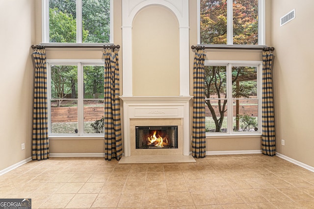 unfurnished living room featuring visible vents, baseboards, and a warm lit fireplace
