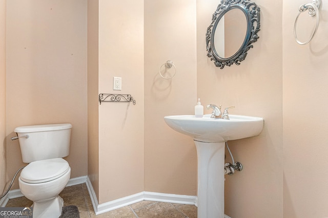 half bath featuring toilet, baseboards, a sink, and tile patterned flooring