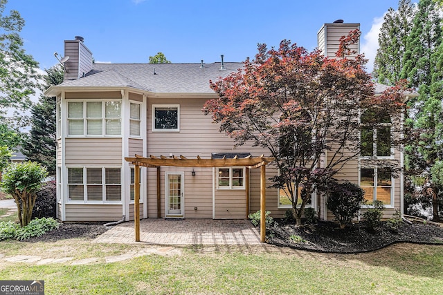 rear view of property featuring roof with shingles, a pergola, a chimney, a lawn, and a patio