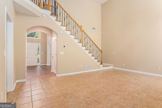 foyer with visible vents, stairs, baseboards, a high ceiling, and arched walkways