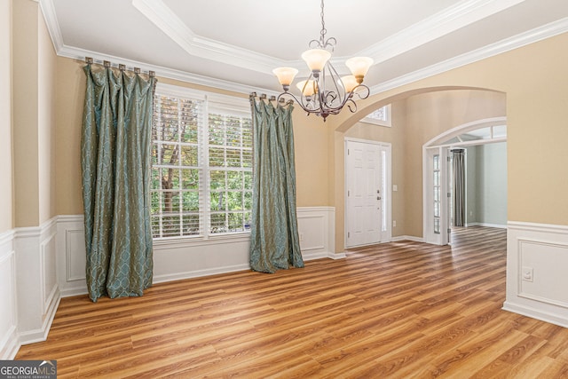 unfurnished dining area with crown molding, light wood-style floors, a wainscoted wall, a chandelier, and arched walkways