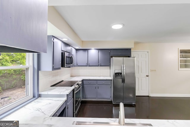 kitchen featuring light stone countertops, tasteful backsplash, a sink, gray cabinetry, and stainless steel appliances