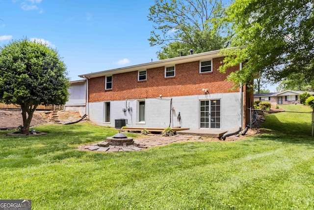 back of property with a fire pit, fence, central AC, brick siding, and a yard