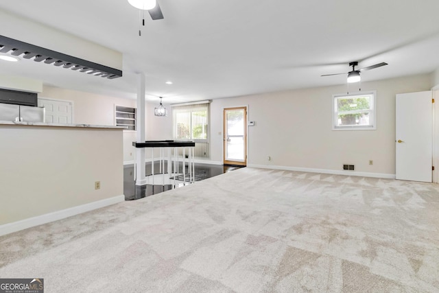 unfurnished living room with carpet floors, a ceiling fan, baseboards, and a wealth of natural light