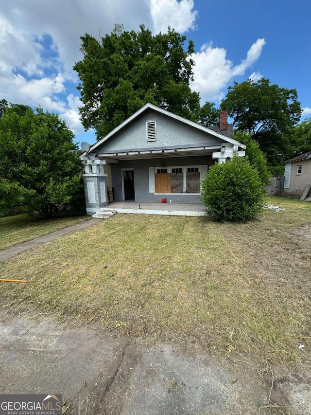 bungalow-style home with a porch, a front lawn, and a chimney