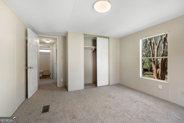 unfurnished bedroom with carpet floors, visible vents, multiple windows, and a closet