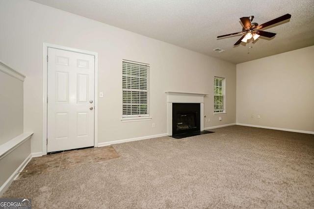 unfurnished living room featuring carpet flooring, ceiling fan, a textured ceiling, a fireplace with flush hearth, and visible vents