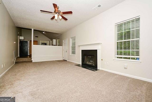unfurnished living room with a fireplace with flush hearth, carpet, a ceiling fan, and visible vents