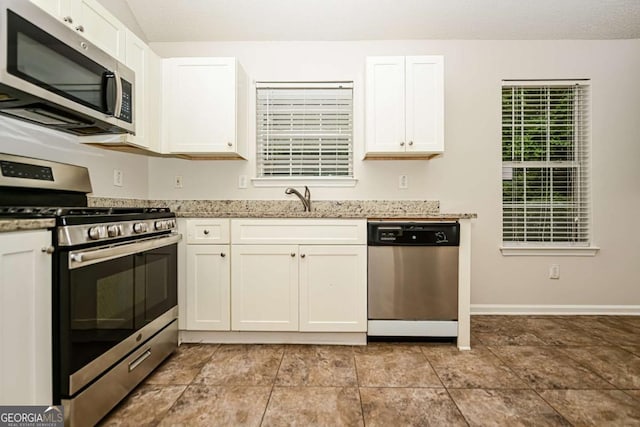 kitchen with light stone countertops, baseboards, white cabinets, a sink, and appliances with stainless steel finishes