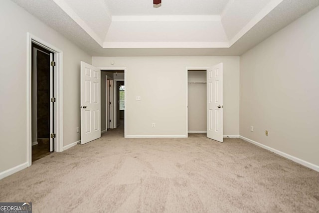 unfurnished bedroom with a closet, baseboards, light carpet, and a tray ceiling