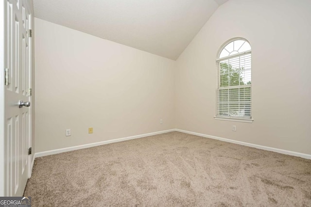 carpeted spare room featuring baseboards and vaulted ceiling