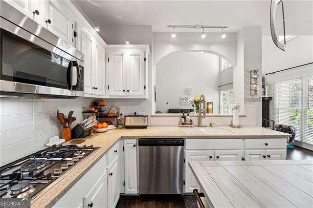 kitchen with track lighting, white cabinets, tasteful backsplash, a sink, and appliances with stainless steel finishes