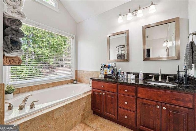 full bathroom with double vanity, a bath, tile patterned flooring, vaulted ceiling, and a sink