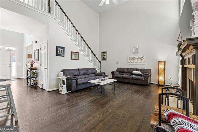 living area with dark wood-style flooring, a fireplace, stairs, baseboards, and a towering ceiling