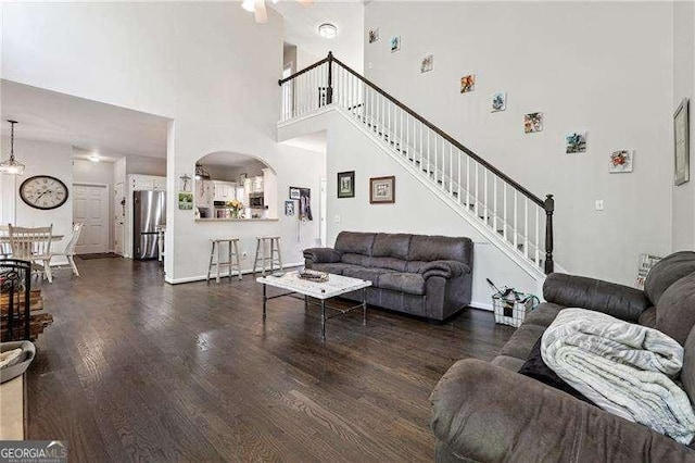 living room featuring wood finished floors, baseboards, a high ceiling, stairway, and arched walkways