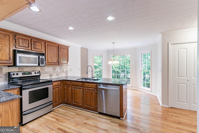 kitchen with brown cabinetry, ornamental molding, a peninsula, a sink, and stainless steel appliances