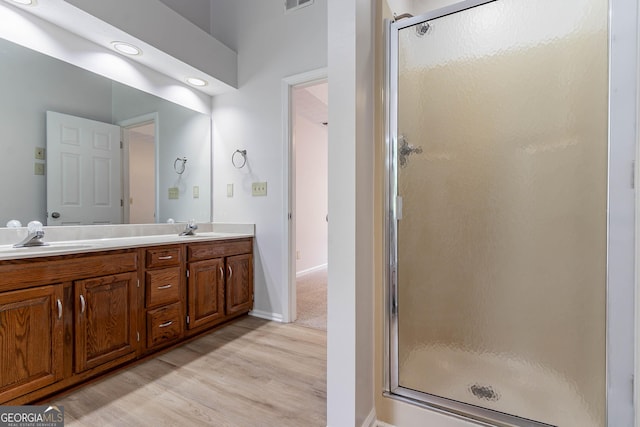 bathroom featuring double vanity, a sink, wood finished floors, and a shower stall