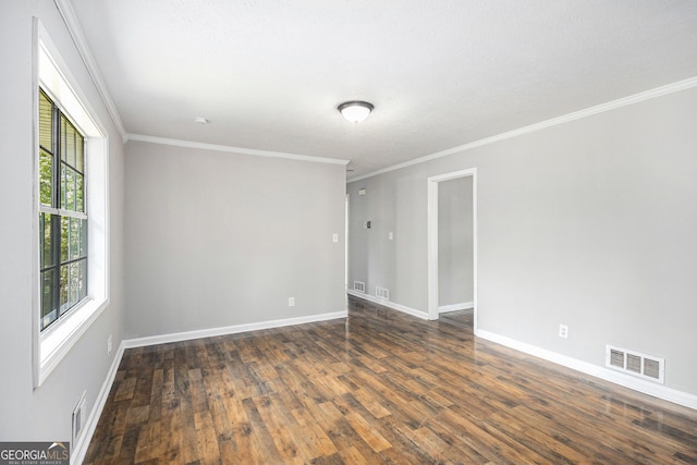 empty room with visible vents, baseboards, crown molding, and dark wood-style floors
