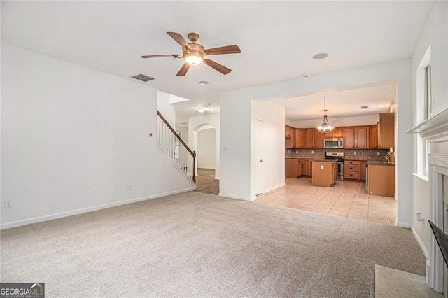 7454 Silver Arrow Trl SE, Austell, GA 30168 - unfurnished living room with light carpet, a fireplace with flush hearth, stairs, ceiling fan, and arched walkways