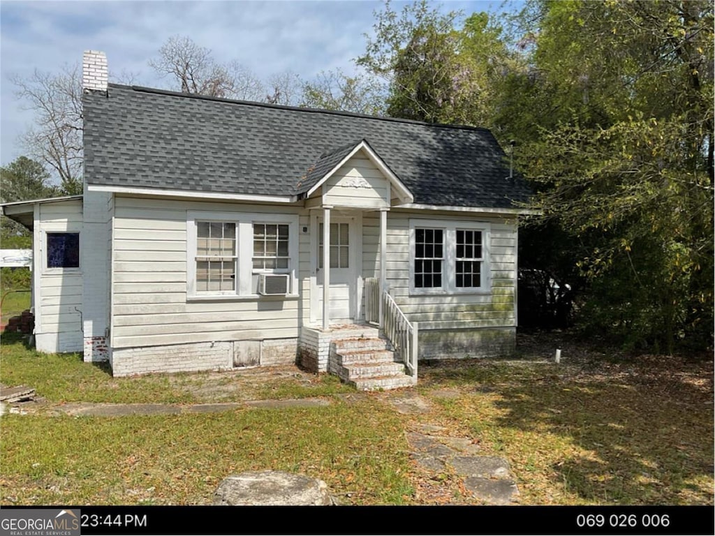 view of front of house with a front yard, cooling unit, and roof with shingles