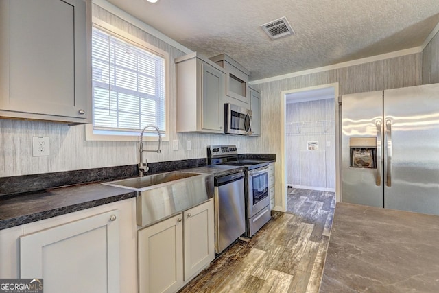 kitchen featuring a textured ceiling, appliances with stainless steel finishes, dark countertops, a sink, and dark wood-type flooring