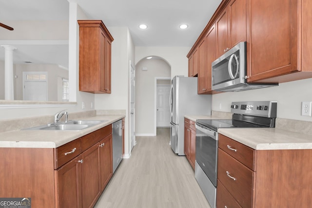 kitchen featuring brown cabinetry, light countertops, arched walkways, light wood-style flooring, and stainless steel appliances