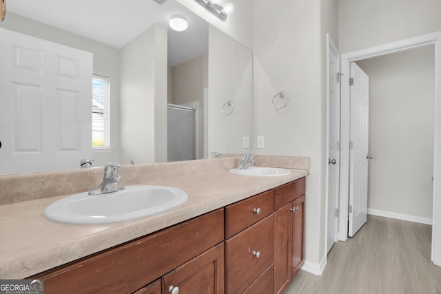 bathroom featuring double vanity, a shower stall, a sink, and wood finished floors