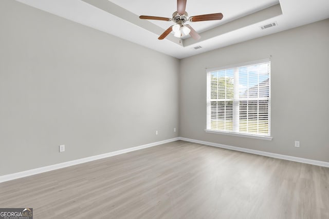 empty room featuring baseboards, a tray ceiling, light wood finished floors, and visible vents