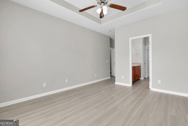unfurnished room with light wood-style floors, a ceiling fan, baseboards, and a raised ceiling