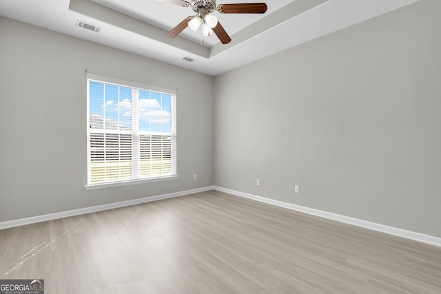 spare room featuring visible vents, a raised ceiling, baseboards, and light wood-style floors