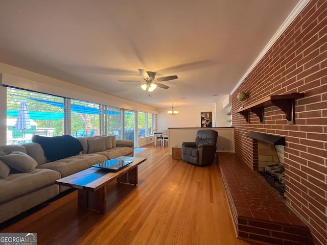 living area featuring a fireplace, ceiling fan with notable chandelier, light wood finished floors, and brick wall