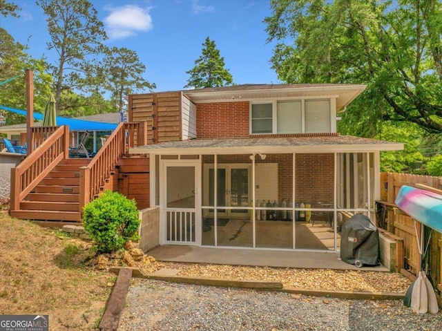 rear view of house featuring fence, stairs, a shingled roof, brick siding, and a sunroom