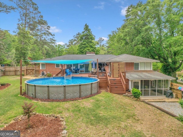 rear view of house featuring a sunroom, a deck, an outdoor pool, a fenced backyard, and a lawn