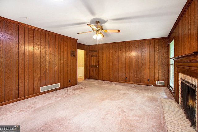 unfurnished living room featuring a brick fireplace, a ceiling fan, visible vents, and wooden walls
