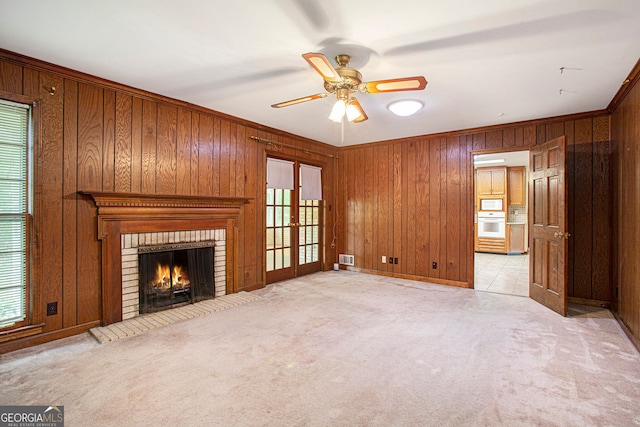 unfurnished living room with a ceiling fan, wood walls, light carpet, and ornamental molding
