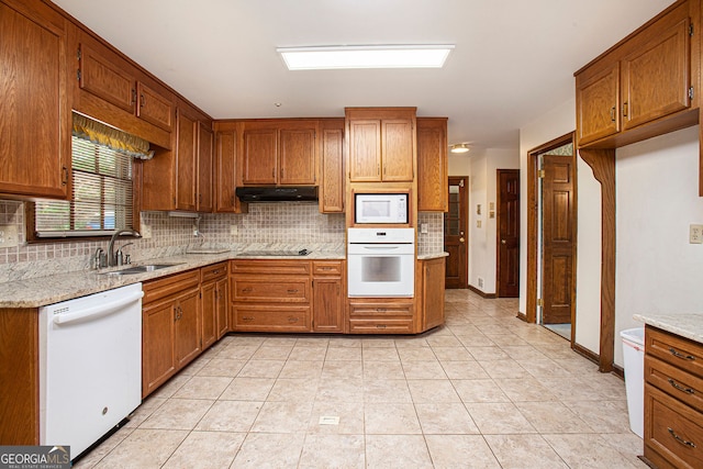 kitchen featuring a sink, tasteful backsplash, brown cabinetry, and white appliances